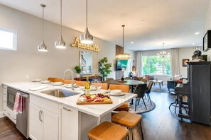 Une cuisine moderne dotée d’un îlot en marbre, de luminaires suspendus et d’un coin repas avec un piano.