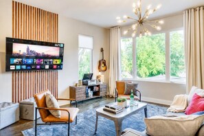 Un salon moderne avec un téléviseur à écran plat, une guitare et une vue sur la verdure à l’extérieur.