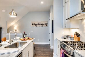 Cozinha moderna com ilha central, eletrodomésticos de aço inoxidável e luminária pendente.