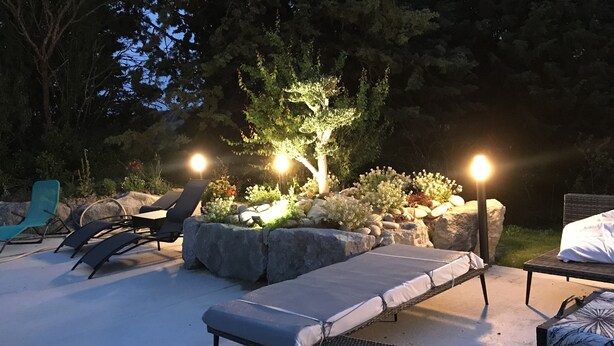 An outdoor seating area with lounge chairs and a small table, surrounded by rocks and plants, with two lights illuminating the space. - Gîte & Bed and Breakfast capacity 14 people with swimming pool, labeled 4 keys. (MAUVAISIN)