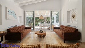 Ein geräumiges Wohnzimmer mit zwei braunen Sofas, einem runden Holztisch und einem großen Fenster mit Blick ins Freie.