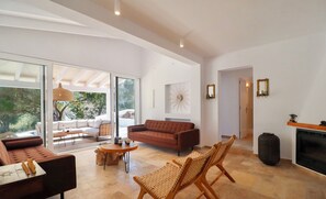 A spacious living area with a brown sofa, wicker chairs, and a coffee table. A fireplace and a large window are visible.
