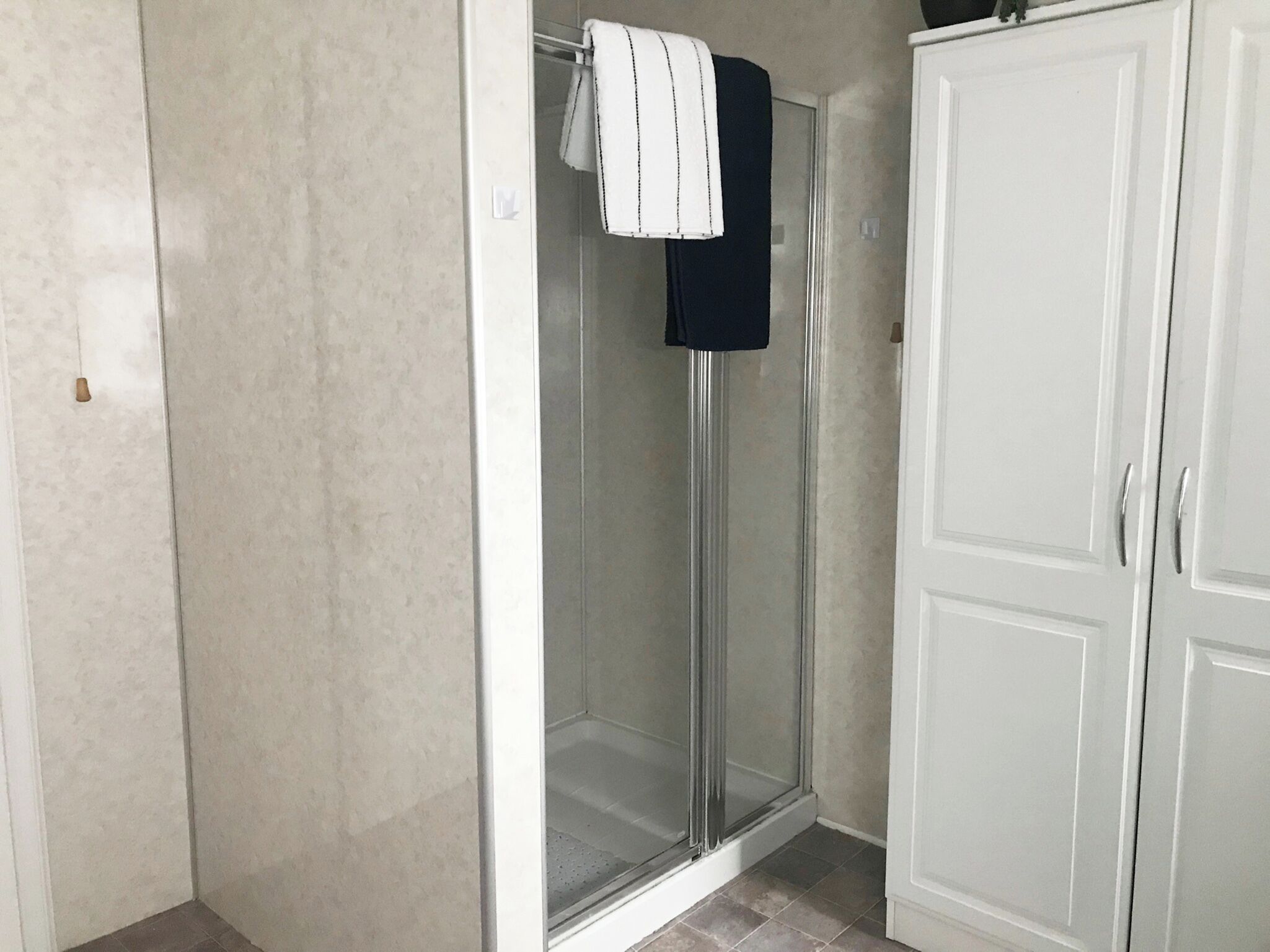 A bathroom with a glass shower enclosure, a white cabinet, and a towel hanging on the shower door.