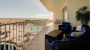 Un balcone con vista sulla spiaggia, un'area salotto con mobili in vimini e una pianta in vaso.
