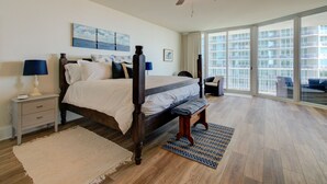 Un'ampia camera da letto con un letto grande, una ventola a soffitto, un comodino con lampade, una finestra vista edificio e un'altra finestra con vista su un balcone.