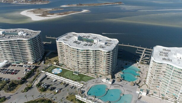 Un hotel di grandi dimensioni con numerosi balconi, un cortile centrale con piscina e vista sull'acqua circostante.