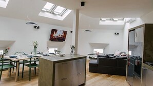 Una cocina moderna con tragaluces, un comedor con sillas verdes y una sala de estar con sofá y televisor.