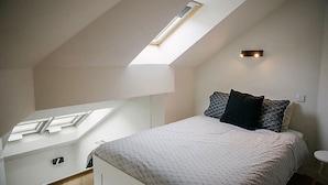 Un dormitorio con tragaluz, una cama con ropa de cama estampada y una mesita de noche pequeña.