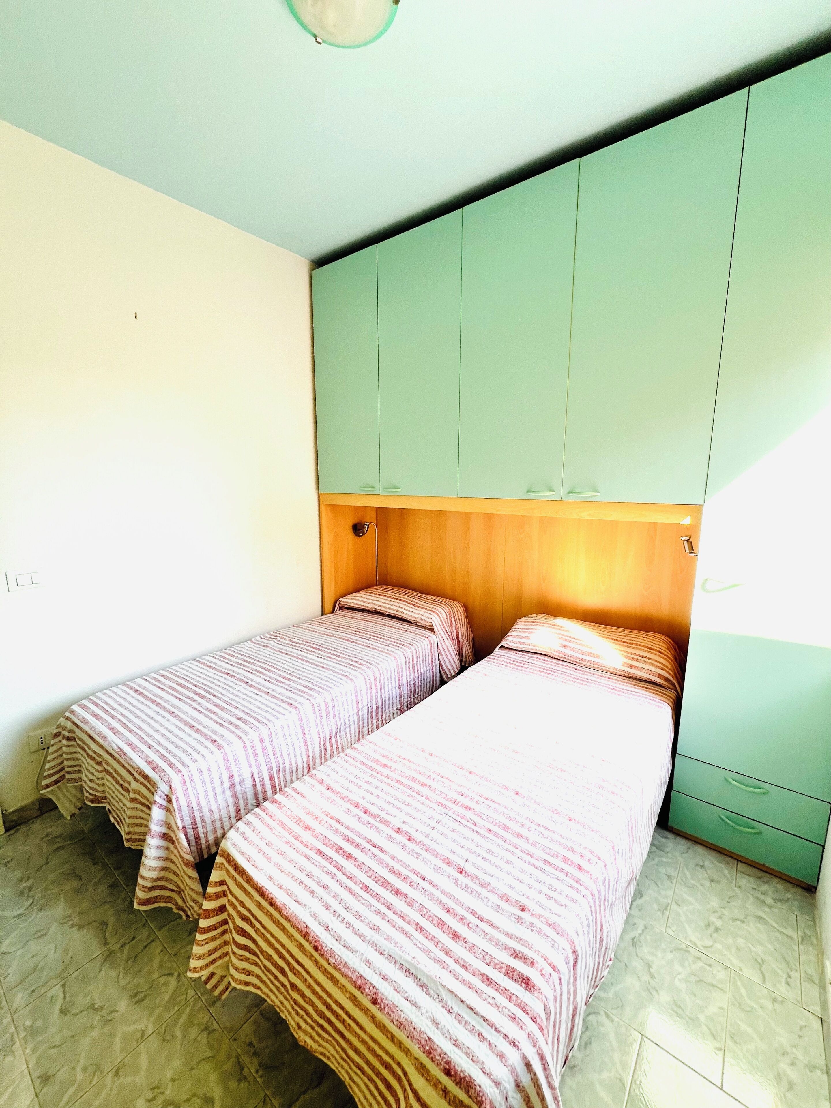 Una habitación pequeña y sencilla con dos camas individuales, un cabecero de madera y un armario verde.
