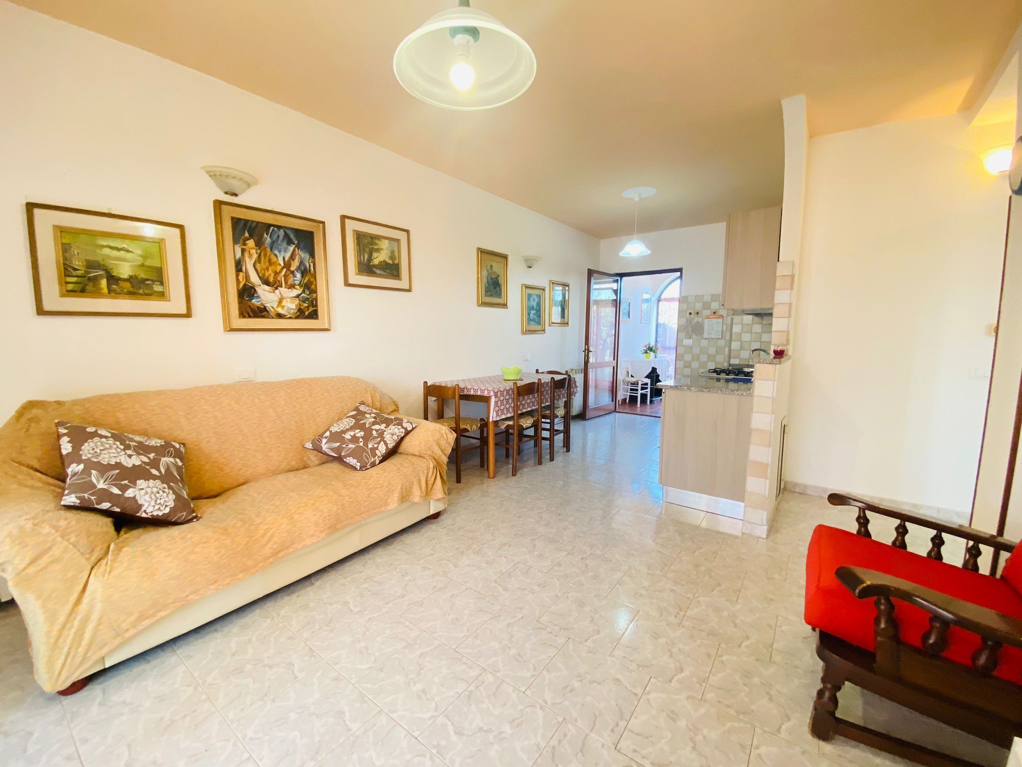 A living room with a sofa, a dining table, and chairs. There is a kitchen area with a stove and cabinets.