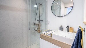 A modern bathroom with a glass-enclosed shower, a round mirror, and a white sink with a wooden countertop.