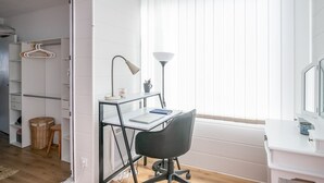 A modern bedroom with a desk, chair, and a large window with blinds.