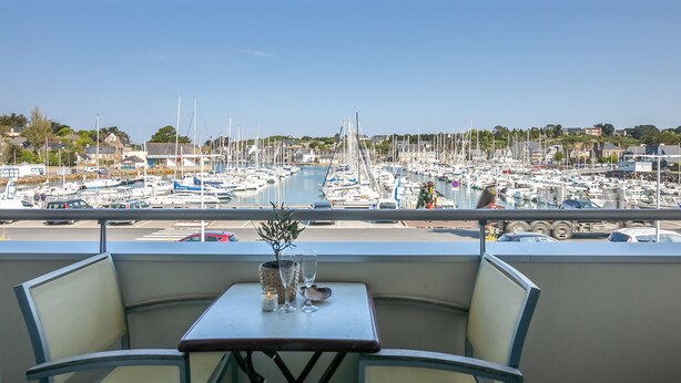 A balcony with a table set for two, overlooking a marina with numerous boats.