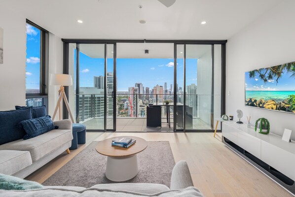 A modern living room with a sofa, coffee table, and a city view through large windows.