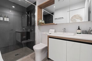A modern bathroom with a glass-enclosed shower, a toilet, a sink, and a mirror with a wooden frame.