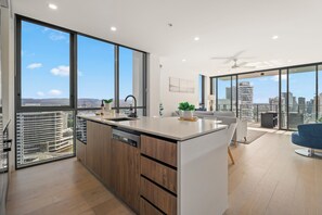 A modern kitchen with a large island, a dining area with a blue chair, and a city view through large windows.