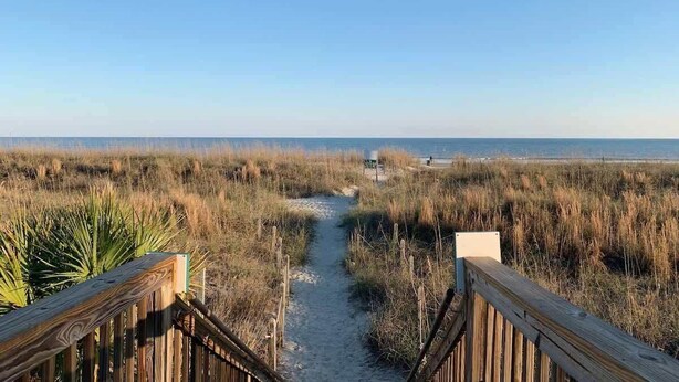 Une promenade en bois qui mène à une plage d’où l’on a une vue dégagée sur l’océan.