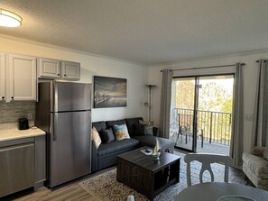 Relax in this cozy living space with a kitchenette, sofa, and balcony offering a view of the surrounding trees.