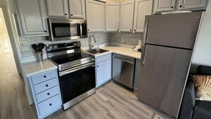 A kitchen with white cabinets, stainless steel appliances, a microwave, oven, sink, and a refrigerator. - Ocean Villa C203 - Balcony Views (Hilton Head Island)