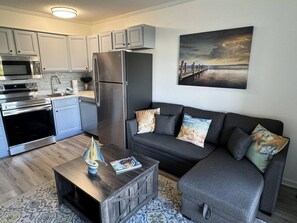 Cozy living space with a kitchen and seating area, featuring a sofa, coffee table, and large painting.