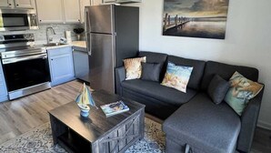A modern kitchen with white cabinets, stainless steel appliances, and a grey sofa with patterned cushions. - Ocean Villa C203 - Balcony Views (Hilton Head Island)