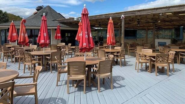 An outdoor seating area with wooden tables and chairs, red umbrellas, and a wooden deck. - Ocean Villa C203 - Balcony Views (Hilton Head Island)