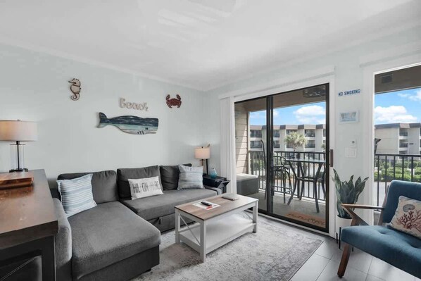 Ein modernes Wohnzimmer mit grauem Sofa, einem Couchtisch und einem Balkon mit Blick auf Gebäude.