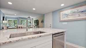 A modern kitchen with a granite countertop, stainless steel sink, and white cabinetry.