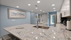A modern kitchen with granite countertops, a stainless steel sink, and recessed ceiling lights.