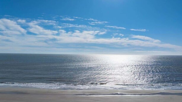 Una platja amb cel blau i sol reflectint a l'aigua.