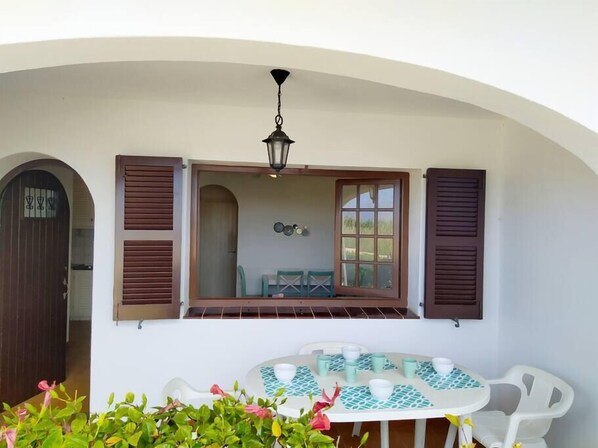 Un patio con tavolo apparecchiato per quattro, circondato da sedie bianche e un lampadario sospeso sopra.