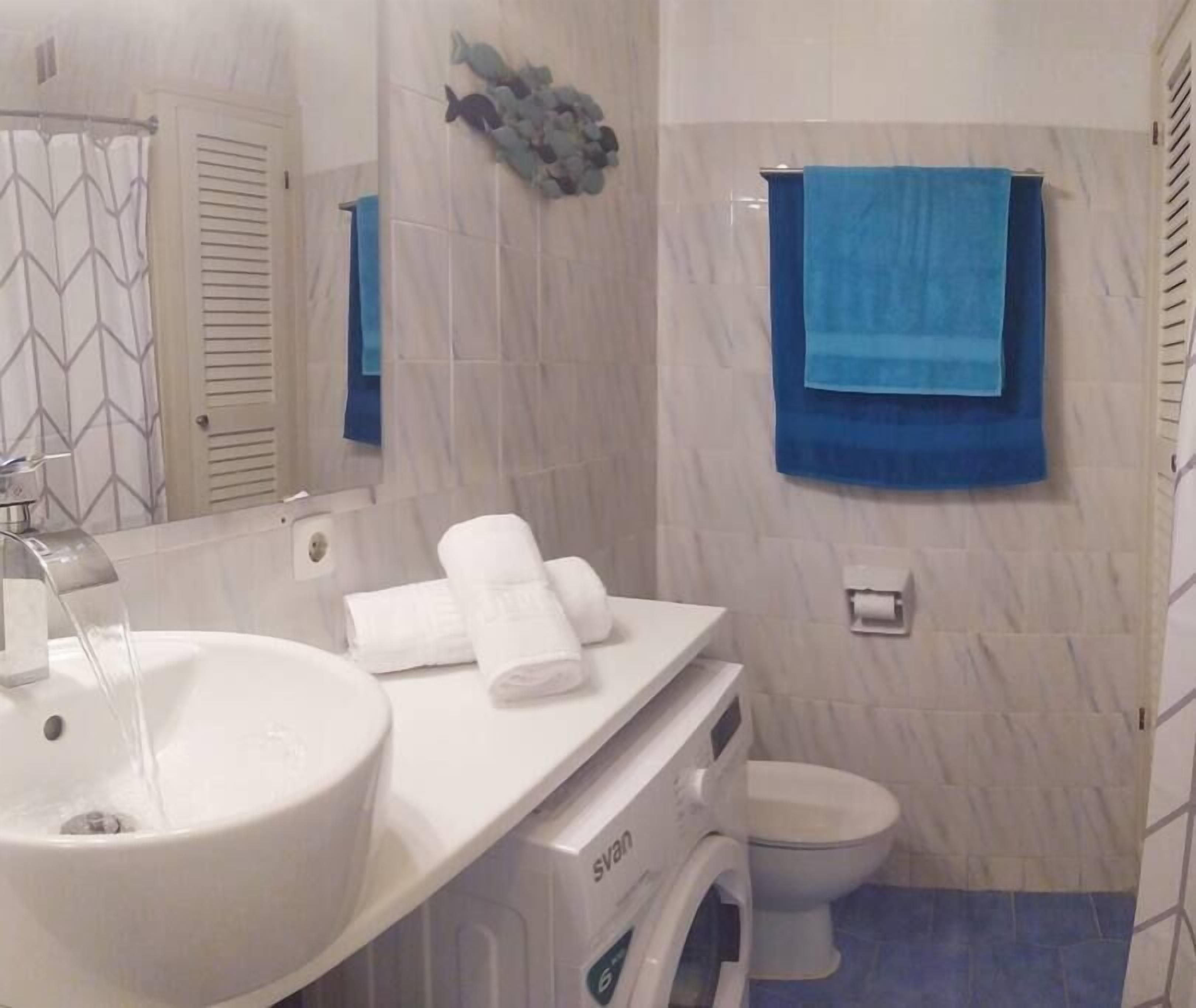Een badkamer met een witte wastafel, een spiegel, een handdoekrek met handdoeken, een toilet en een blauwe handdoek aan de muur.