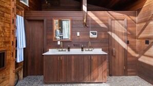 Une salle de bain rustique, avec des murs en bois, dotée d’un lavabo double, de meubles en bois, d’un miroir et d’une serviette accrochée au mur.