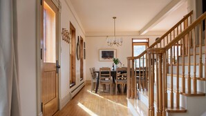 Un couloir avec un plancher en bois, un coin repas avec une table et des chaises, un escalier avec des rampes en bois et un lustre.