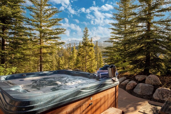 Un jacuzzi rodeado de árboles y rocas, con montañas al fondo.
