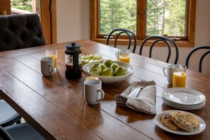 Ein Holztisch mit Frühstücksangebot, darunter eine Schüssel mit grünen Äpfeln, eine Kaffeemaschine und ein Glas Orangensaft.