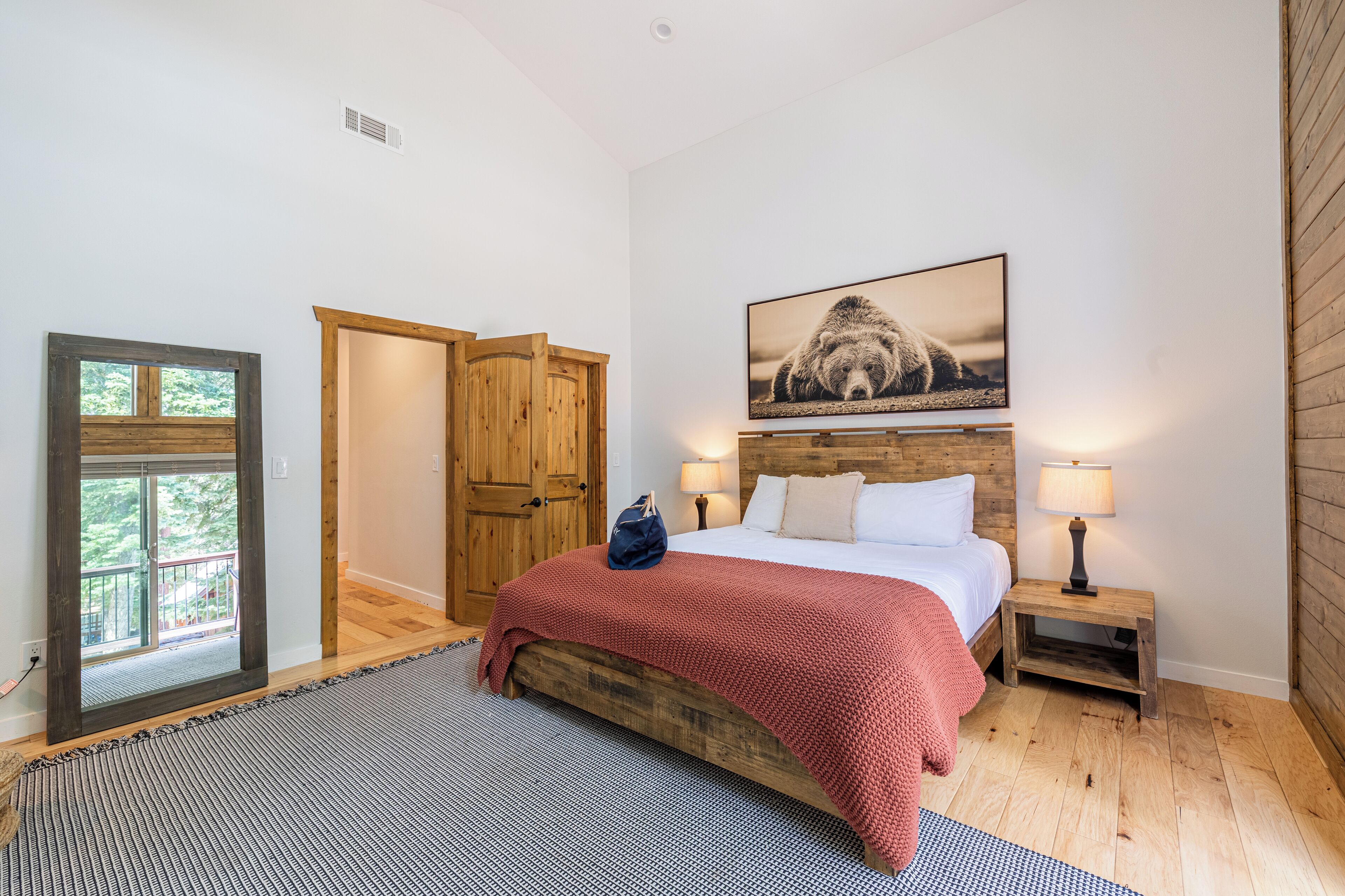 A bedroom with a wooden bed, a large window, a wooden wardrobe, and a bear picture on the wall.