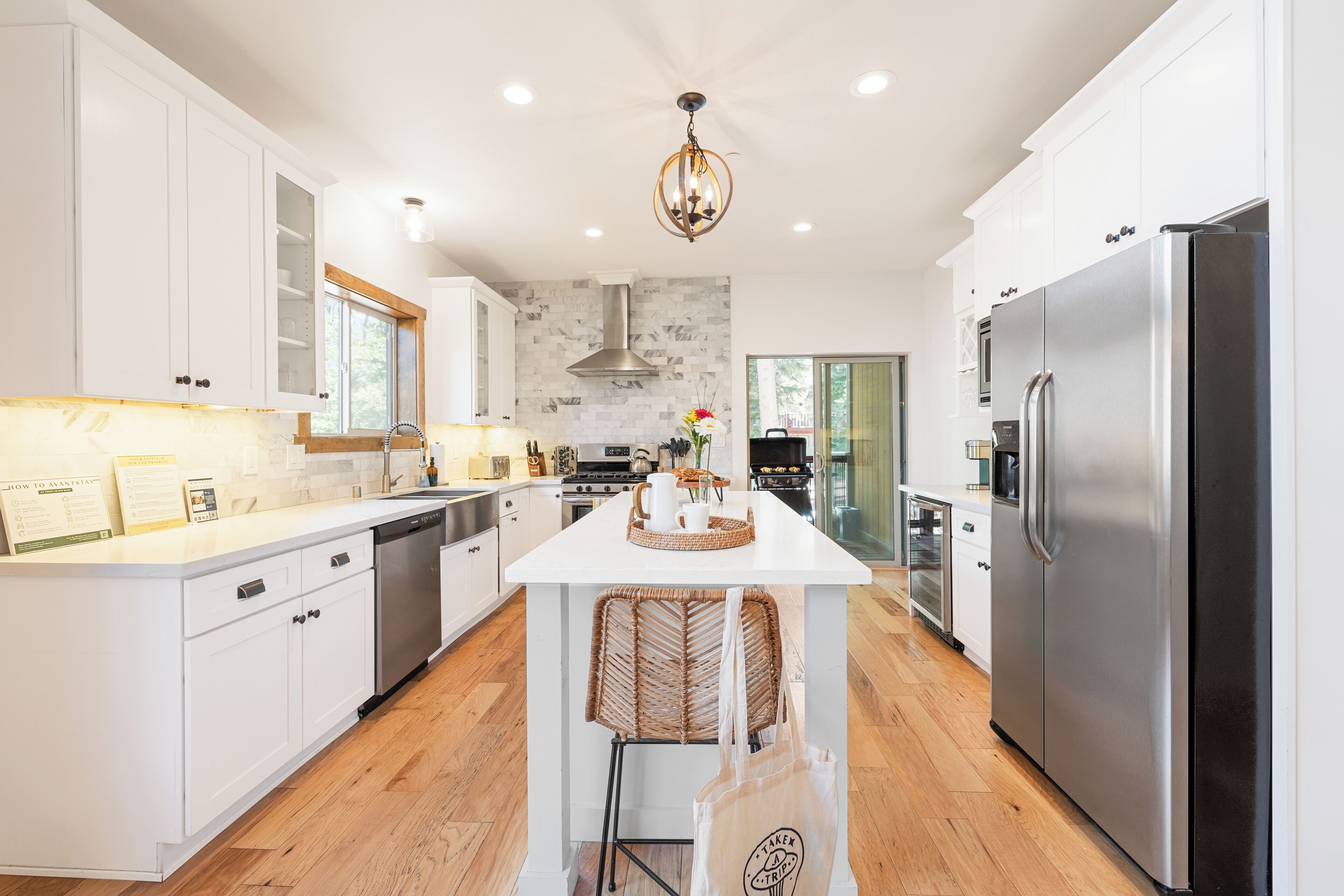 A modern kitchen with white cabinetry, a central island, stainless steel appliances, and a chandelier.