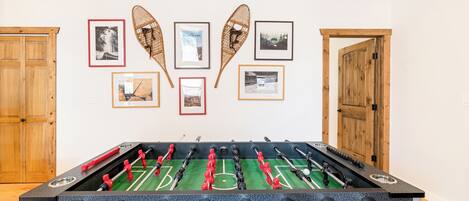 Una mesa de fútbol de mesa en una habitación con puertas de madera y cuadros en la pared.