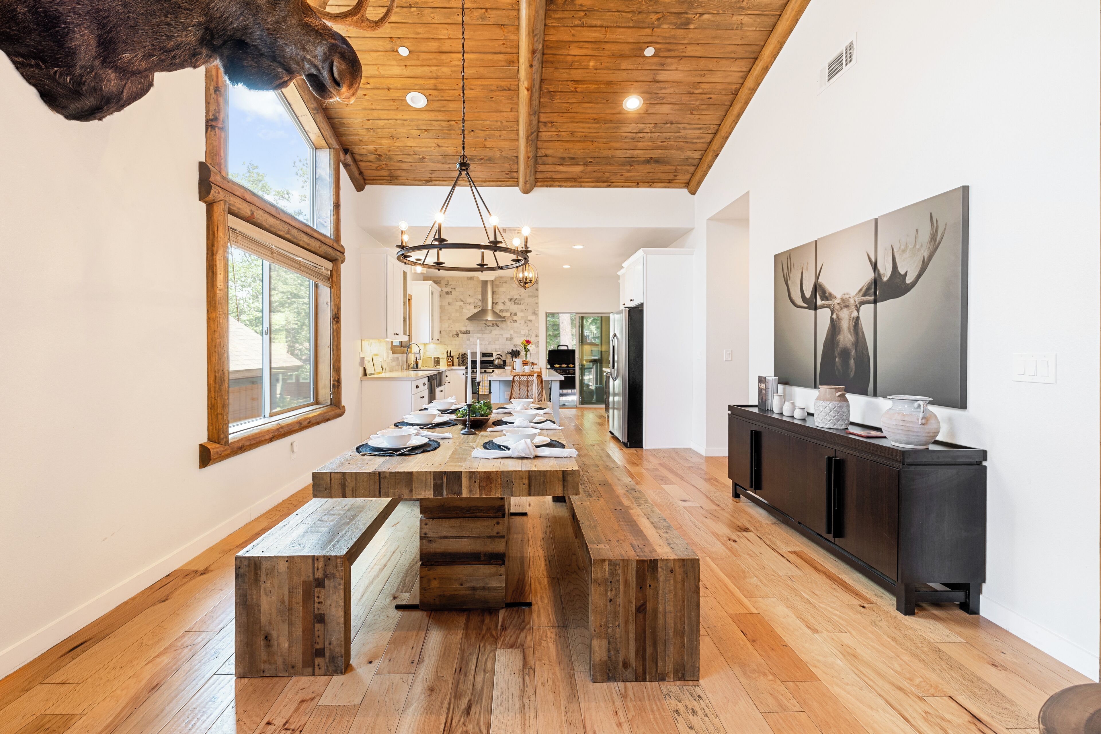 A spacious kitchen with a wooden dining table, a chandelier, and a large deer painting on the wall.