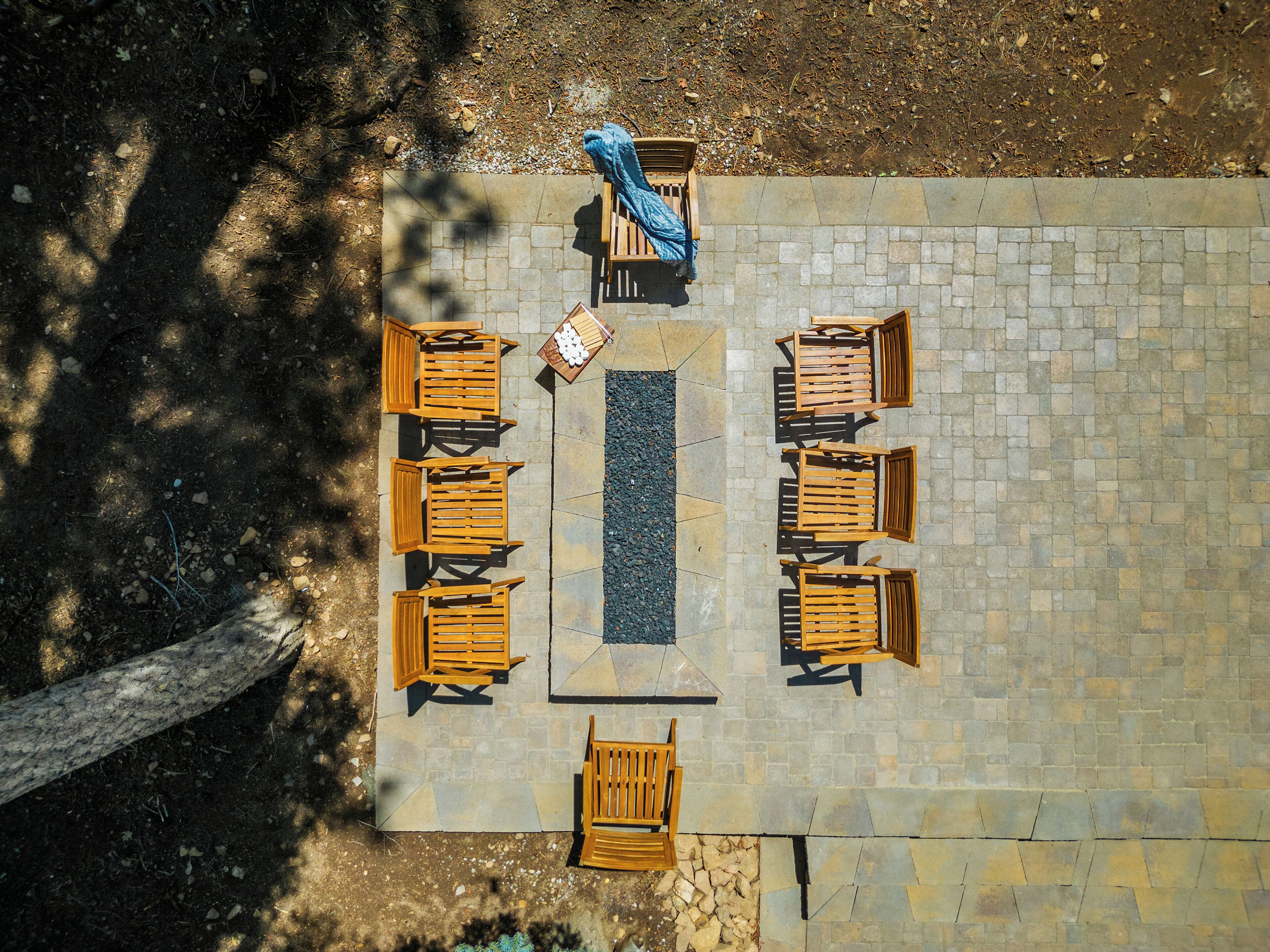 An outdoor seating area with wooden tables and chairs arranged around a central fire pit.