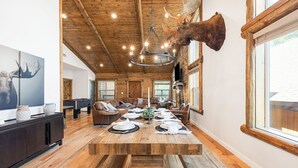 Un comedor amplio con una gran mesa de madera, bancos y una cabeza de alce montada en la pared.