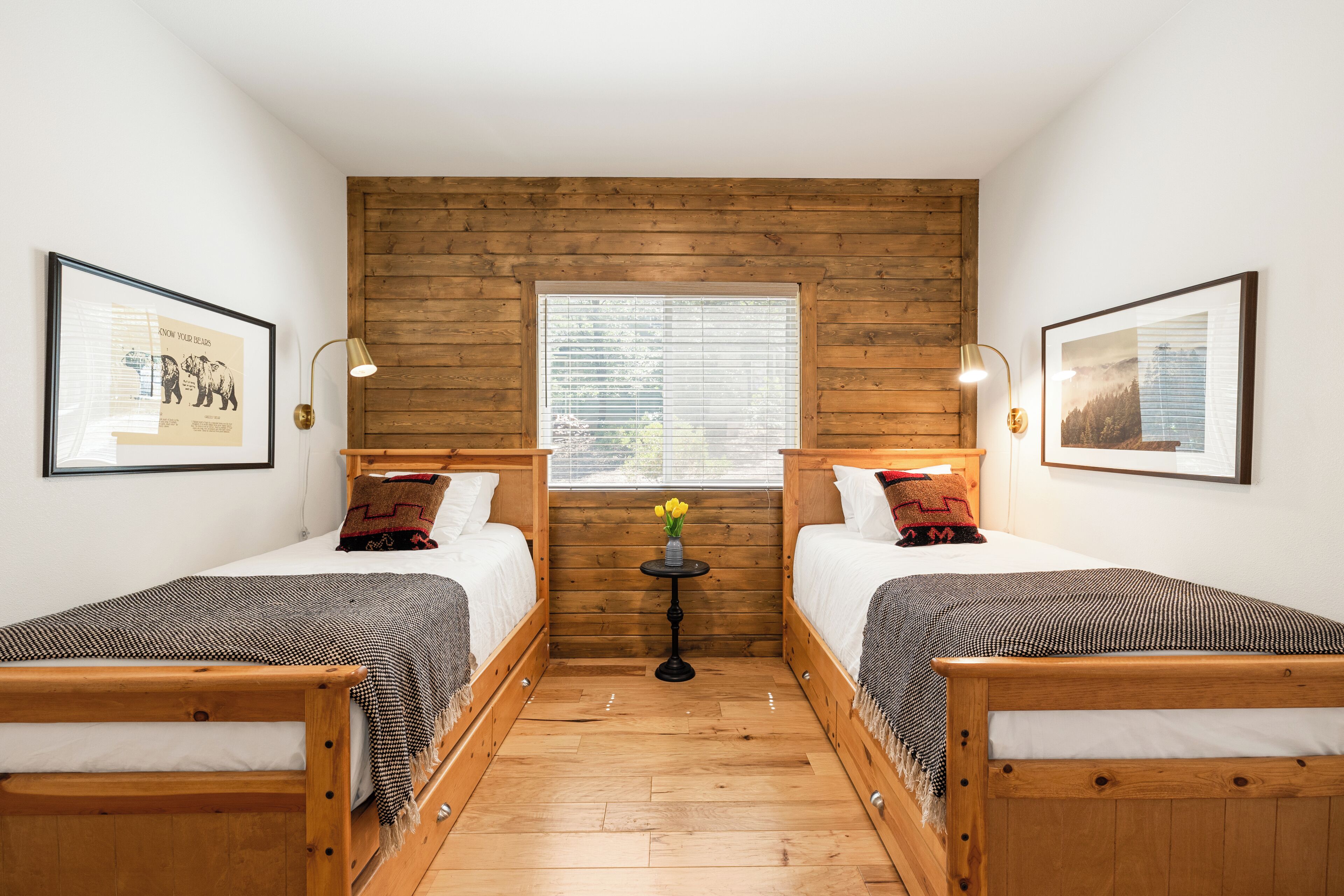 A room with two wooden beds, a small table with a vase of flowers, and framed pictures on the walls.