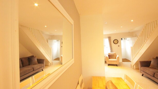 A modern living room with a wooden dining table, two sofas, a white armchair, and a staircase with white railings. - Fantastic 2-bed House in Hull. Garden, Sky tv (Hull)
