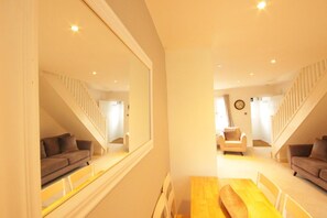 Una sala de estar moderna con una mesa de comedor de madera, dos sofás, un sillón blanco y una escalera con barandillas blancas.