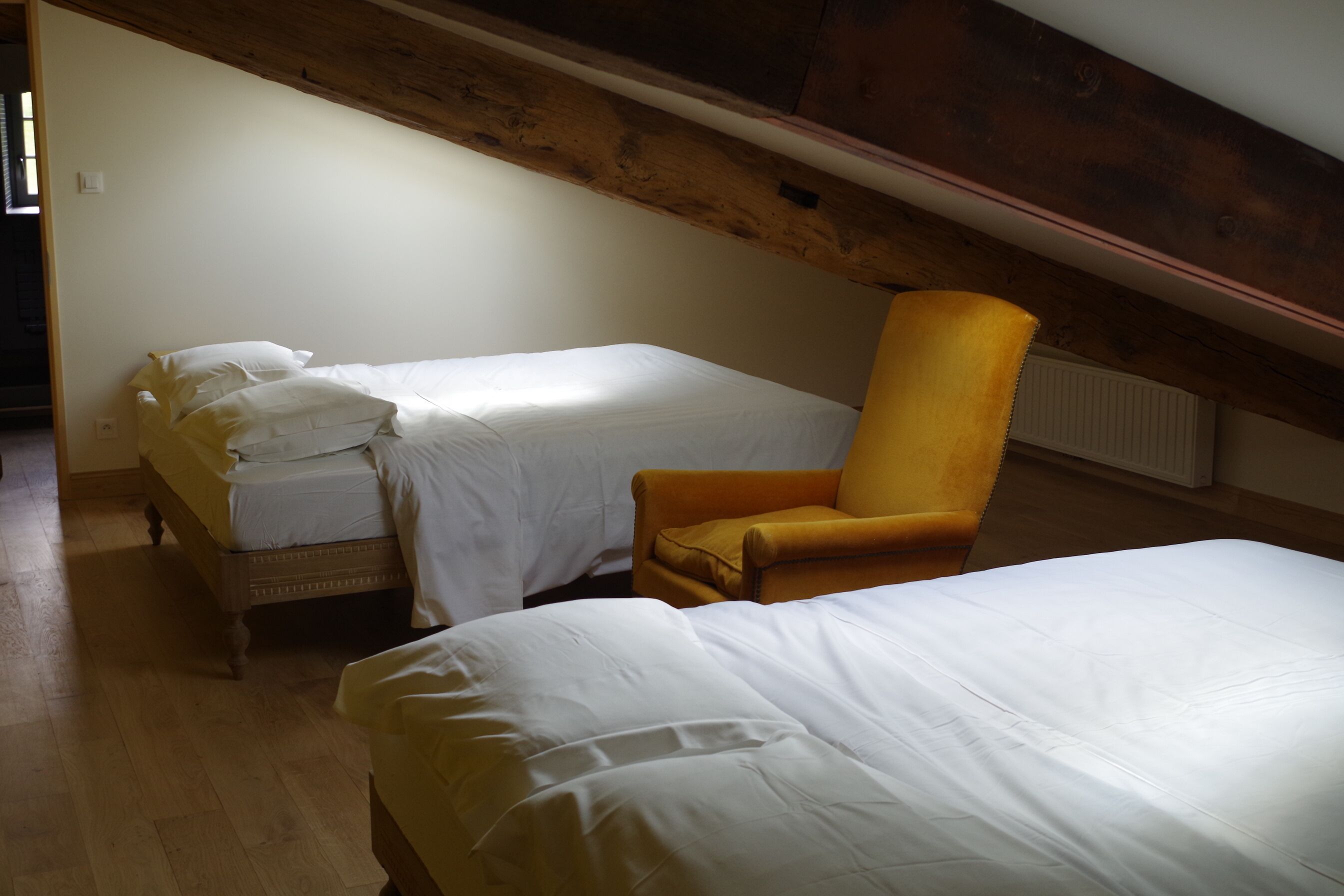 A room with two beds and a single yellow armchair.