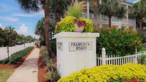 Un panneau de signalisation indiquant « Frangista Beach », avec une clôture en bois peinte en blanc et une végétation luxuriante.