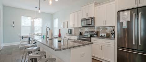 A modern kitchen with white cabinets, stainless steel appliances, and a central island with bar stools.