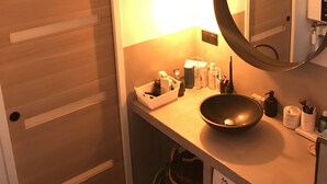 Un baño pequeño con puerta de madera, espejo redondo, lavamanos y lavadora.
