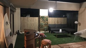 Un patio con terraza de madera, una mesa redonda, dos taburetes de bar, un sofá y una silla blanca.